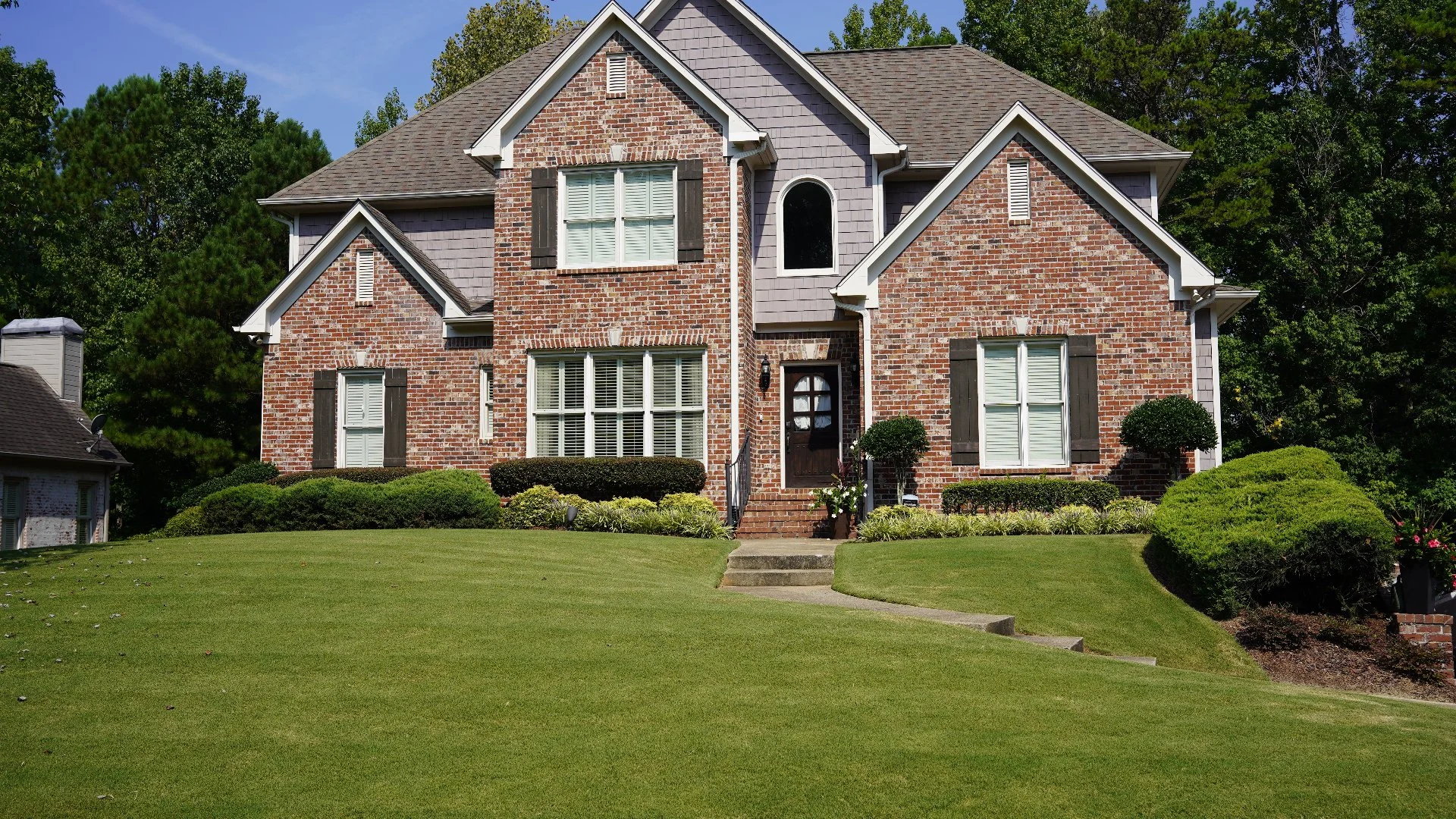 Brick house with green lawn and shrubs.