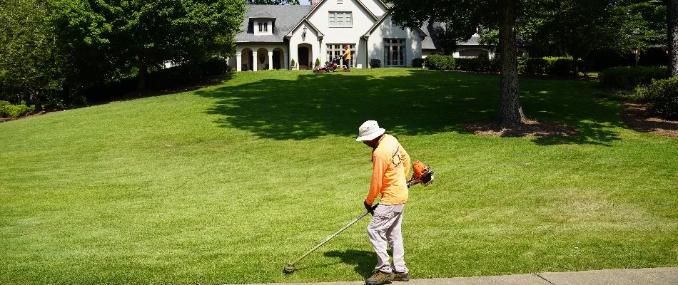 A worker in Mountain Brook, AL, edging along grass on a large lawn.