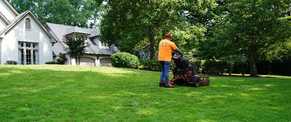 Worker in an orange shirt mowing a lawn in Huntsville, AL.