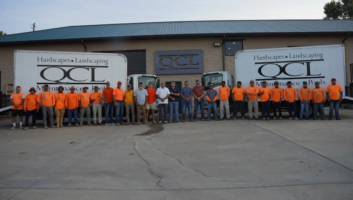 Team members in front of Quality Creative Landscaping trucks.